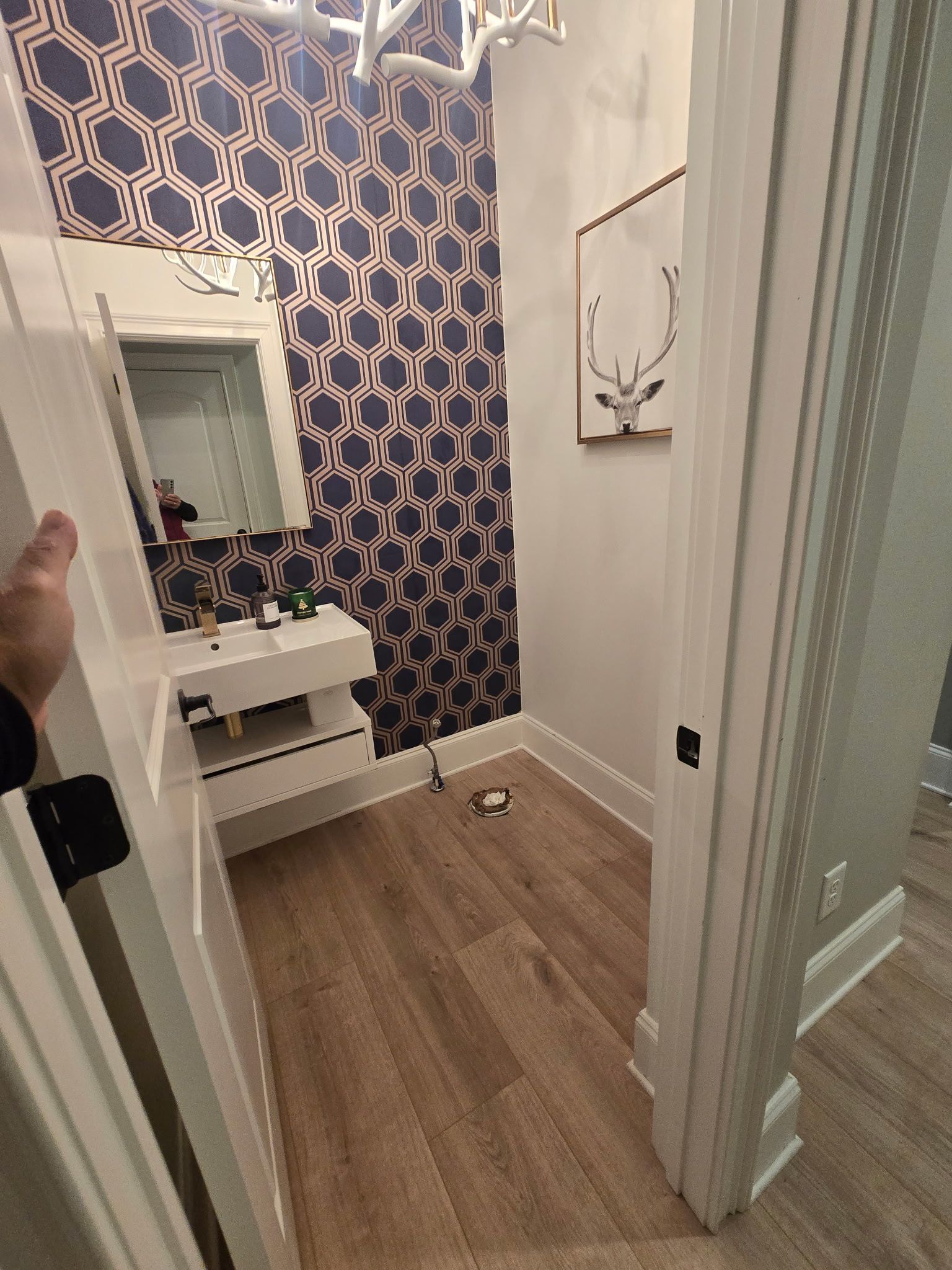 Small bathroom with blue patterned wallpaper, white vanity, wood floor, and glass shower door.
