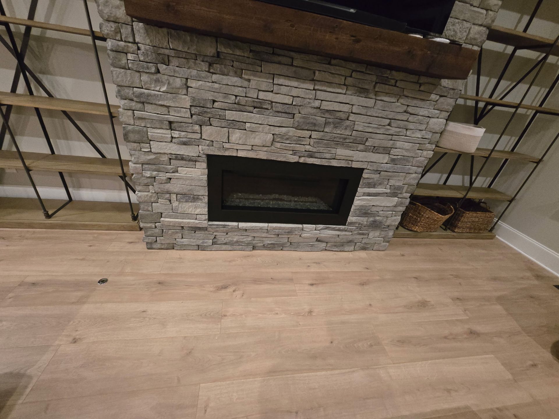 Stone fireplace with wood mantel in a room with light wood flooring and metal stair railings on both sides