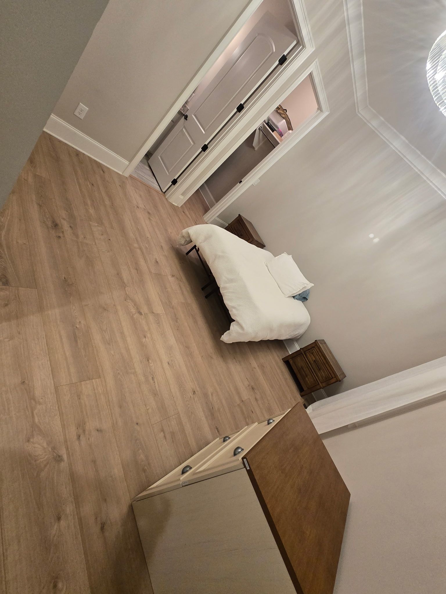 Empty bedroom with wood floors, white walls, a bed, open closet, and a dresser.