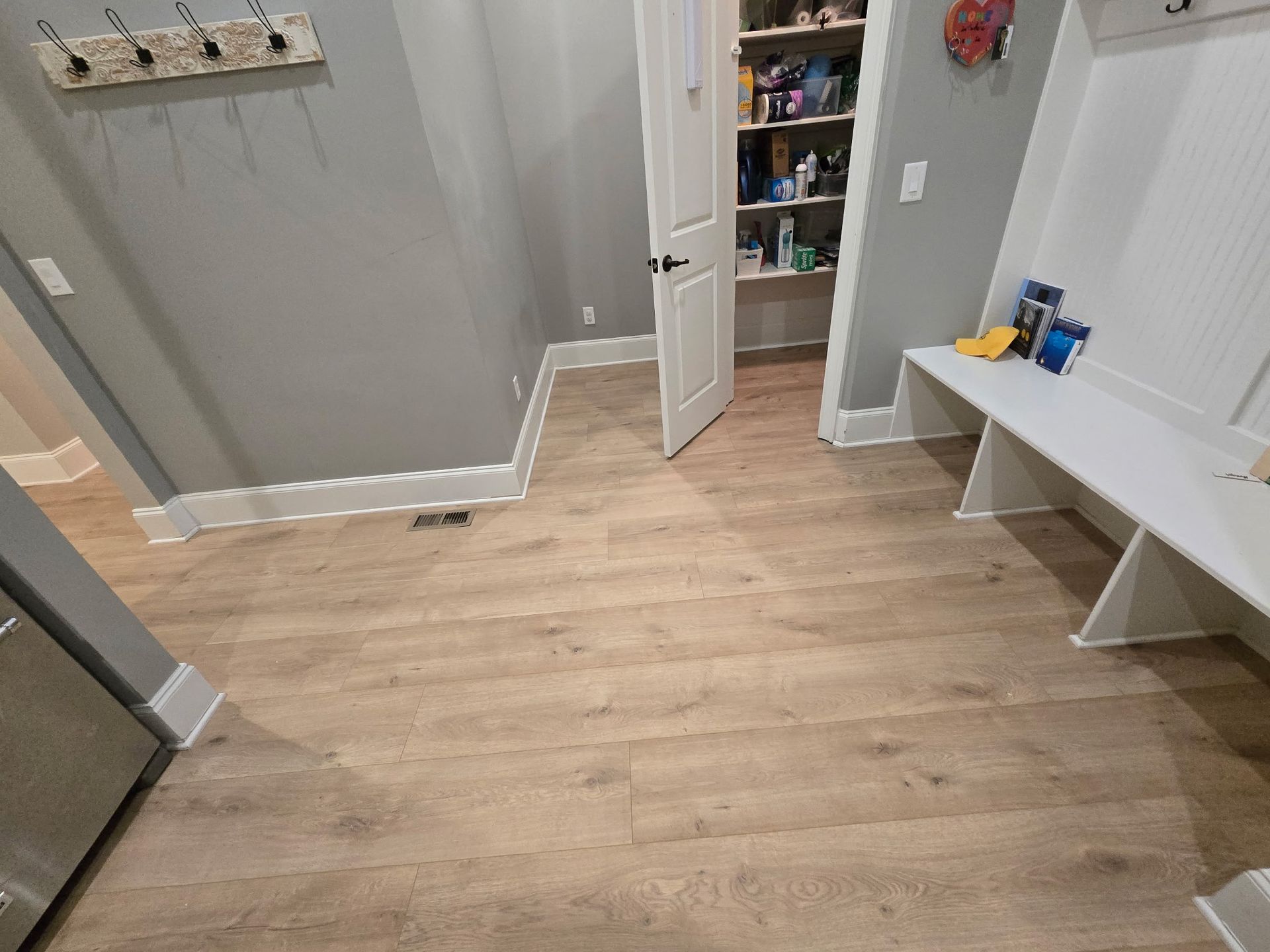 Empty kitchen with light wood flooring, open pantry door, and white bench seating along the wall.