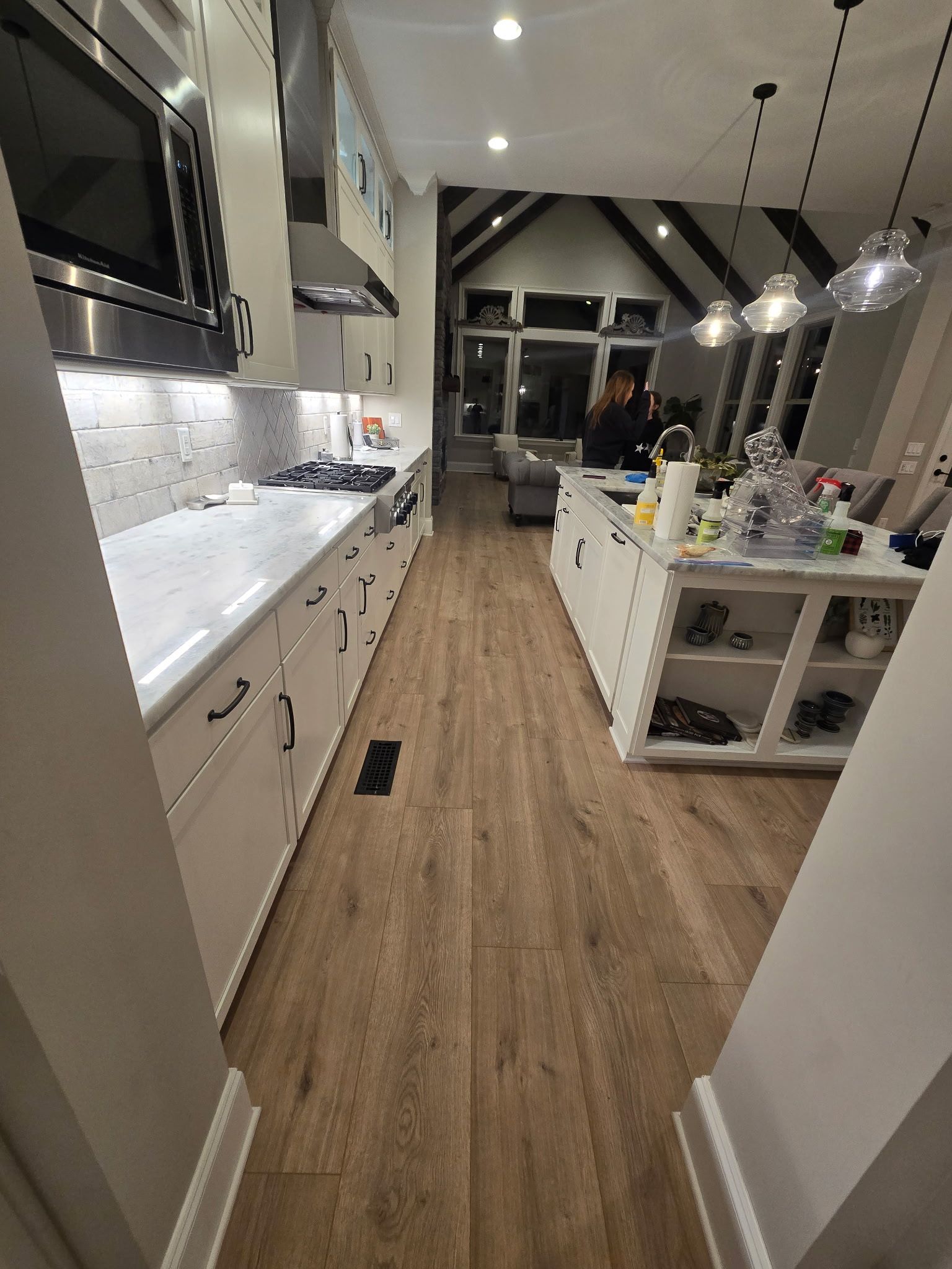 Modern kitchen with white cabinets, wood floors, island, and pendant lights seen from the doorway