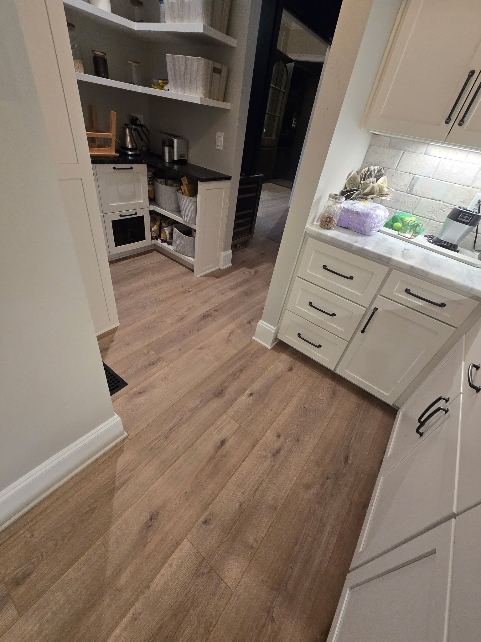 Small kitchen with white cabinets, wood floor, and a sink area leading into a pantry or utility space.