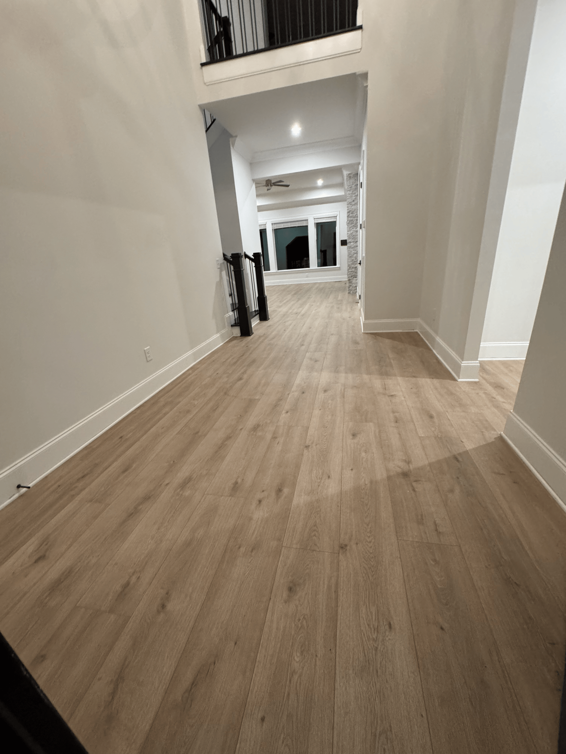 Long hallway with light wood flooring, white walls, and an upper balcony railing.