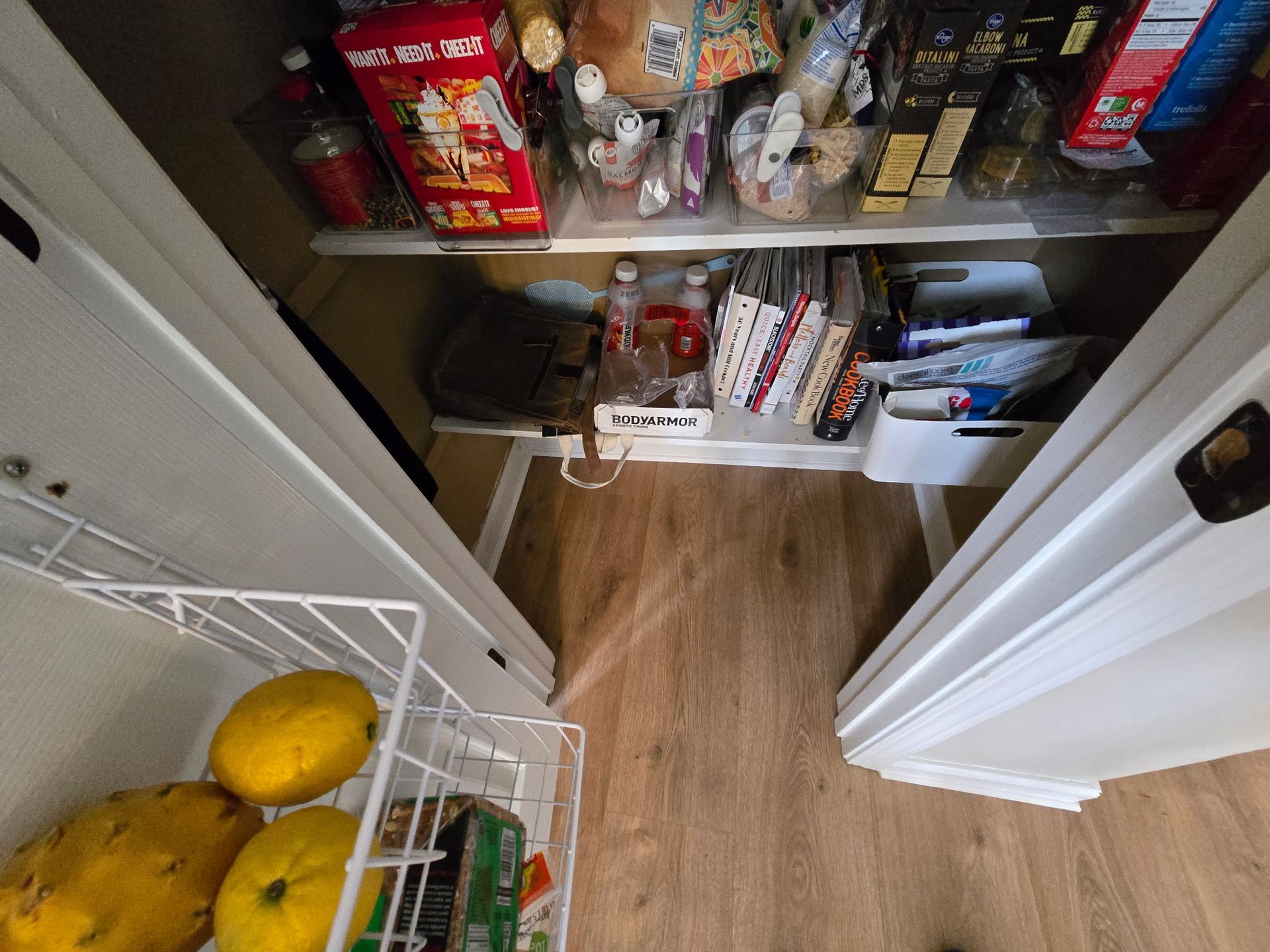 Pantry shelves with assorted food and two melons in a wire basket at the bottom left