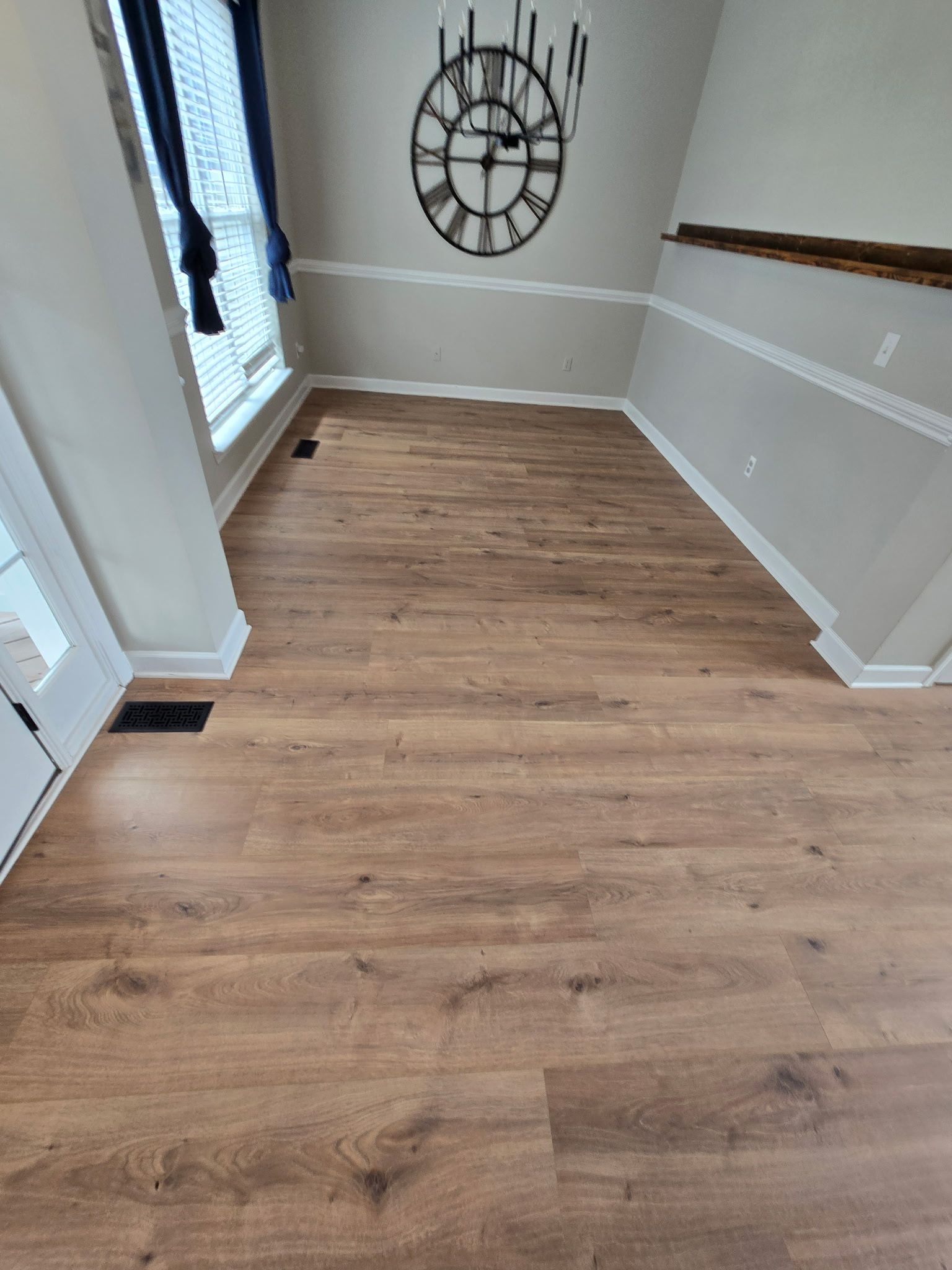 Empty hallway with wood flooring, gray walls, a large wall clock, and a windowed door on the left.