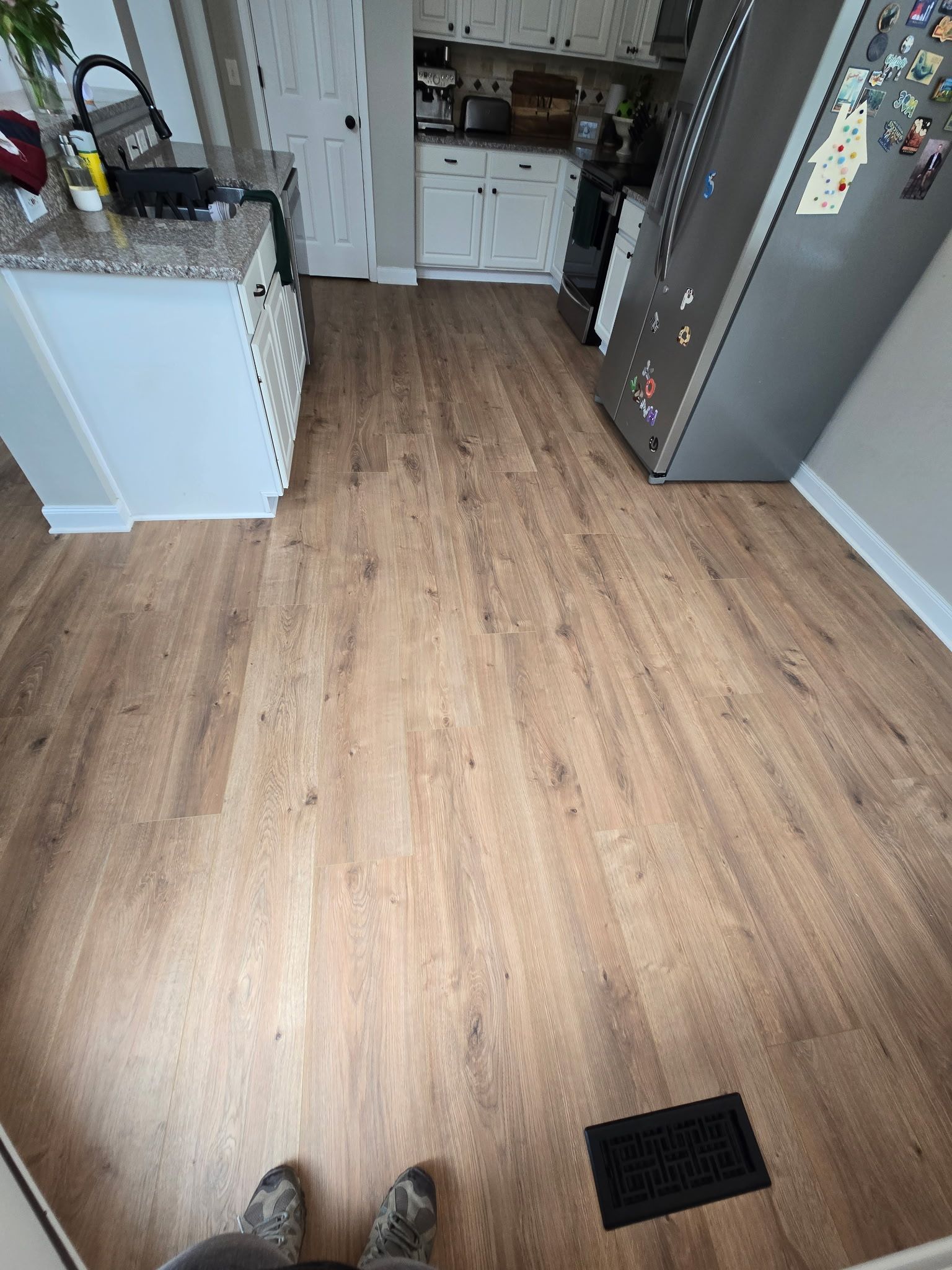 Kitchen with wood-look floor, refrigerator on right, counter on left, and a floor vent near the center.