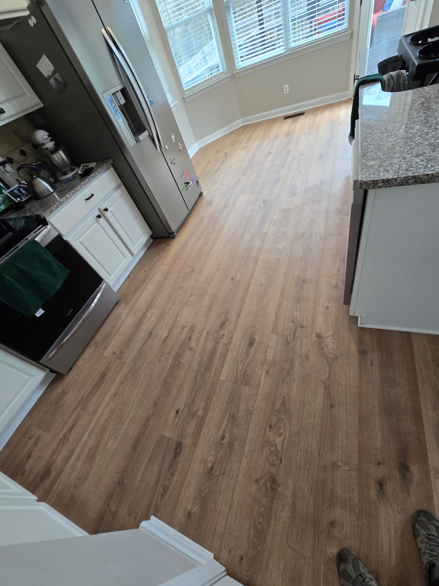 Modern kitchen with light wood flooring, white cabinets, stainless stove, and large windows at the far end