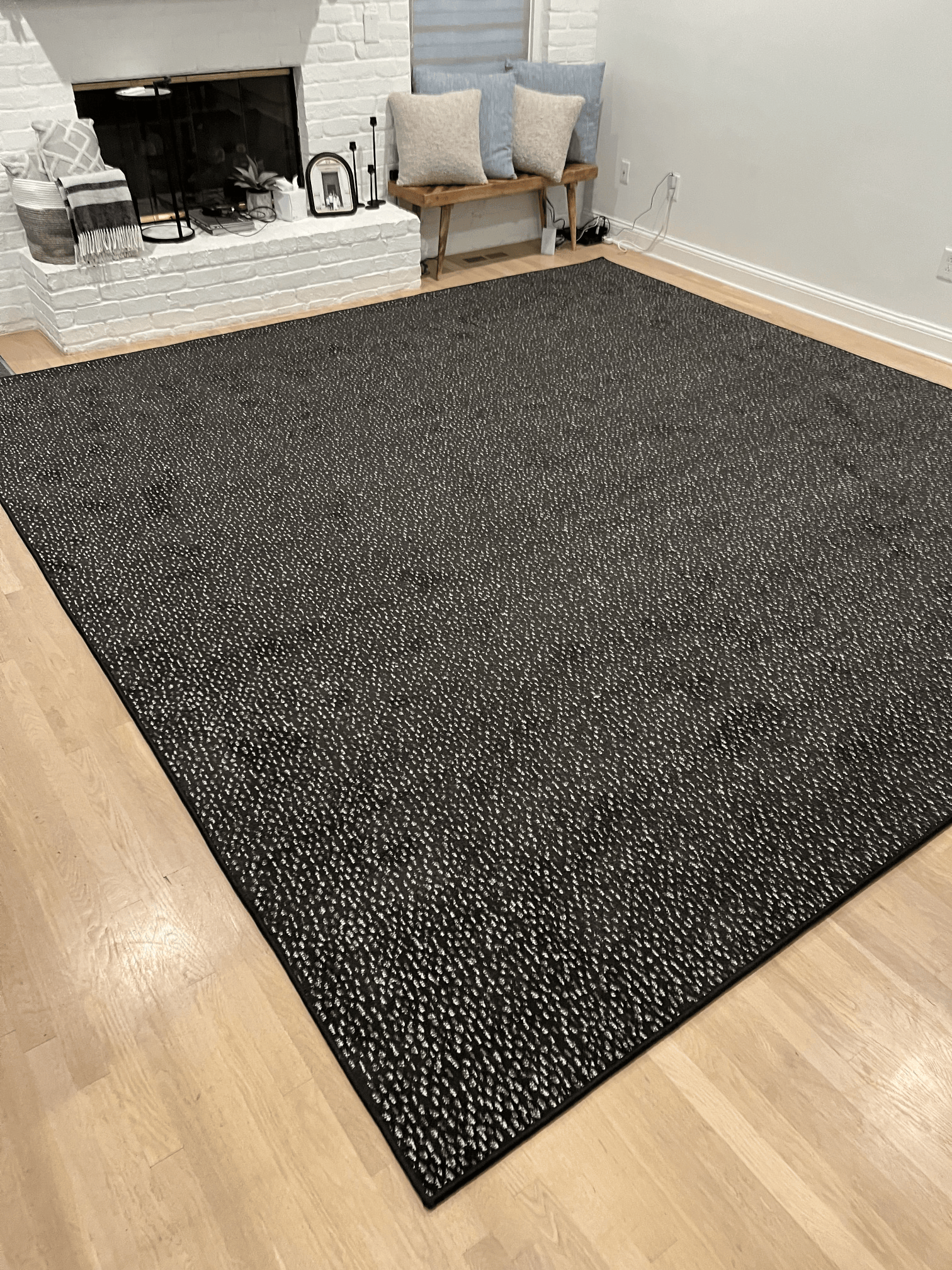 Black speckled area rug on hardwood floor in a living room near a fireplace and chairs