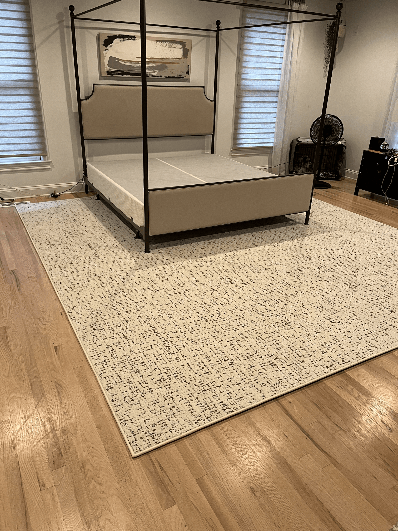 Four-poster bed on a patterned rug in a bright bedroom with wood floors and windows on both sides