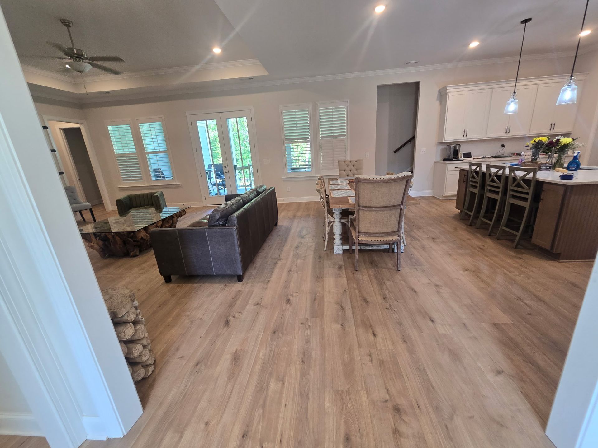 Open-concept living room and kitchen with wood floors, gray sofa, dining table, and island bar stools