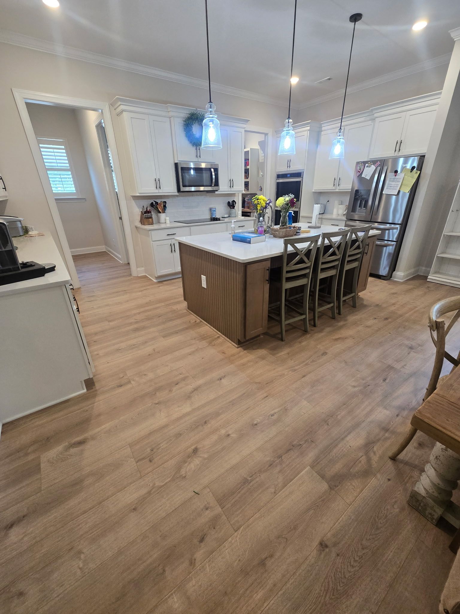 Bright kitchen with island, barstools, stainless fridge, white cabinets, and wood-look flooring