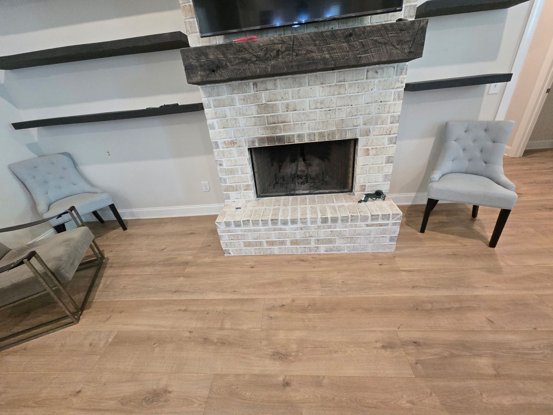 Living room with a brick fireplace, wood floor, and two light blue chairs on either side
