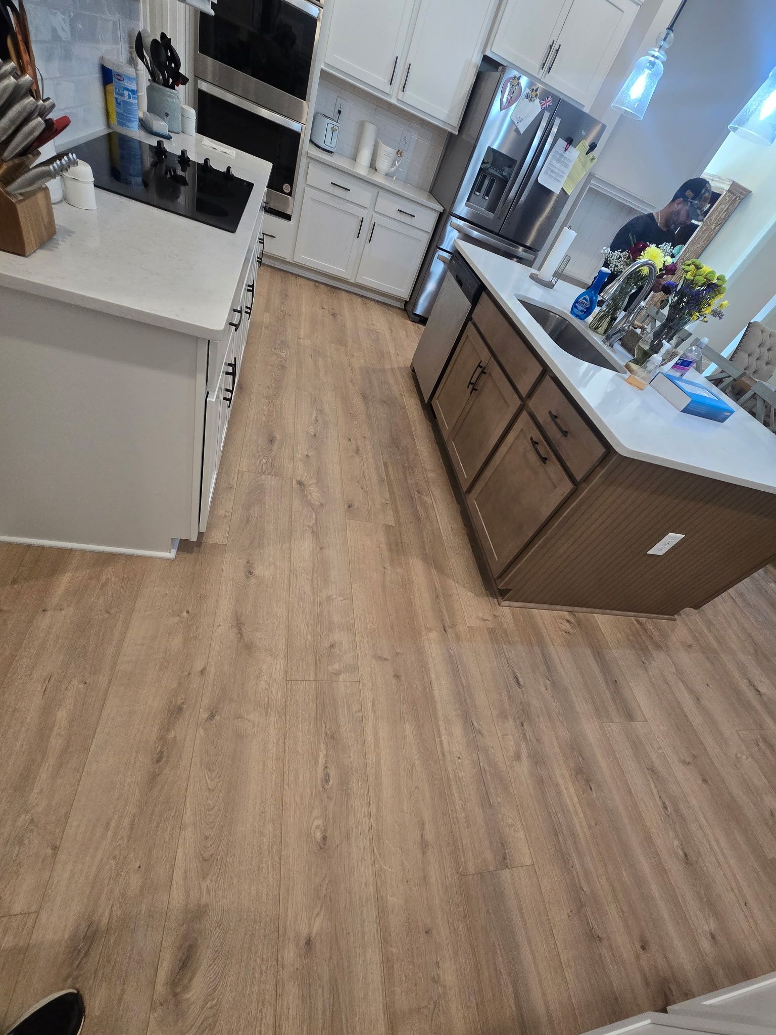 Kitchen with light wood floor, white counters, and brown cabinets; a person stands at the far counter.