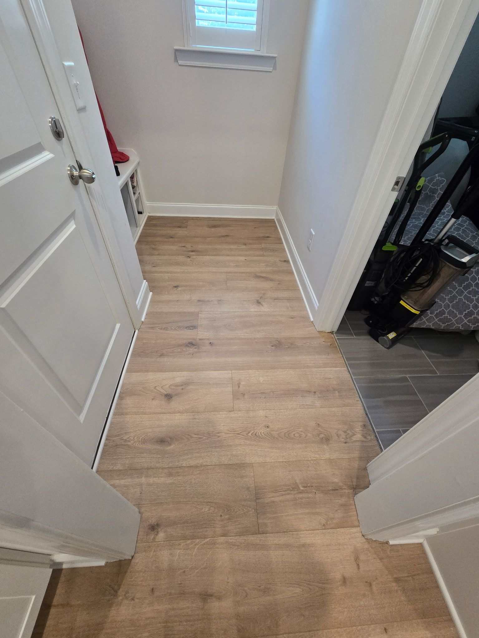 Narrow hallway with wood-look floor leading to a small window, flanked by white walls and doors.