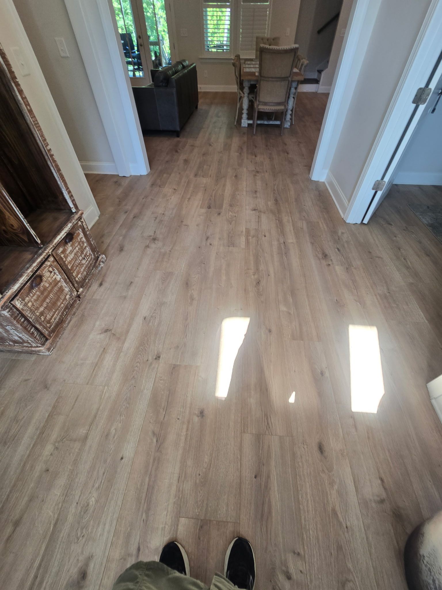Hallway with wood flooring, sunlight on the floor, and a small table and chair at the far end