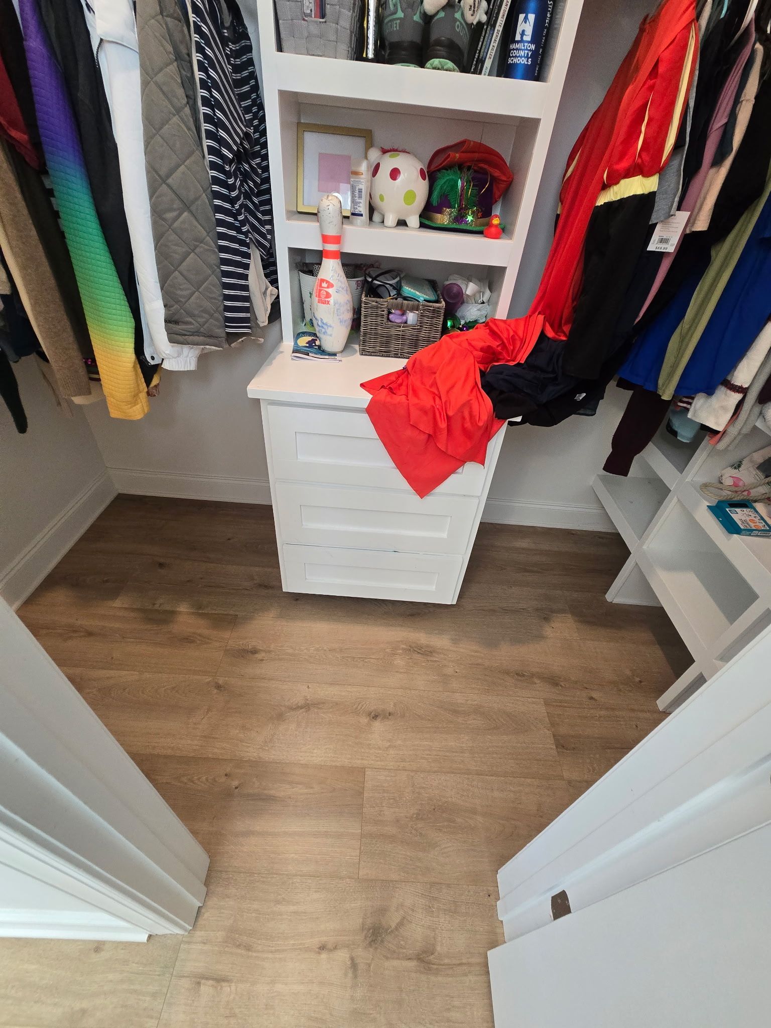 Walk-in closet with hanging clothes and a white drawer unit, with a red shirt draped over it.