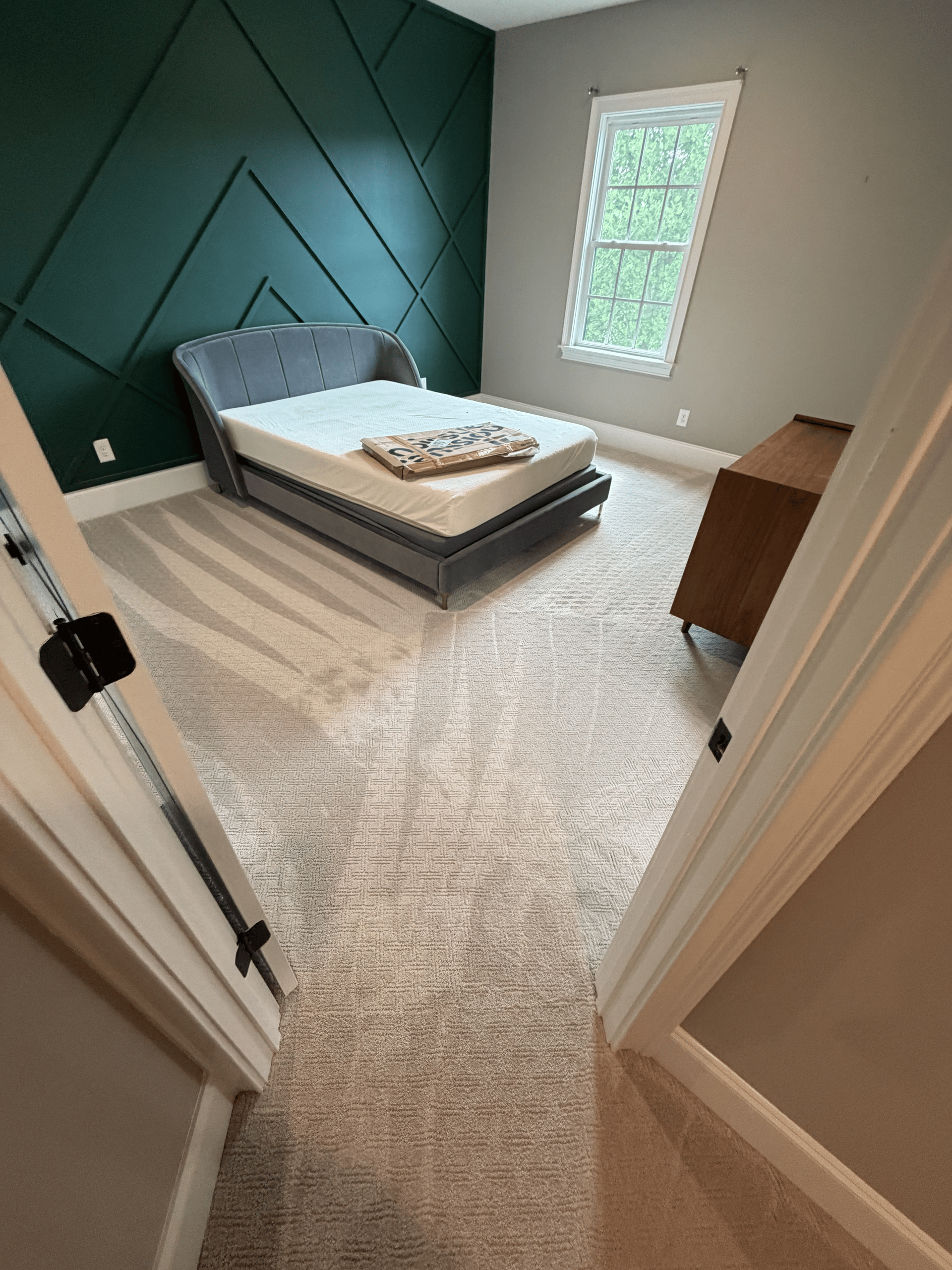Empty bedroom with green accent wall, bed, window, and carpeted floor viewed from the doorway