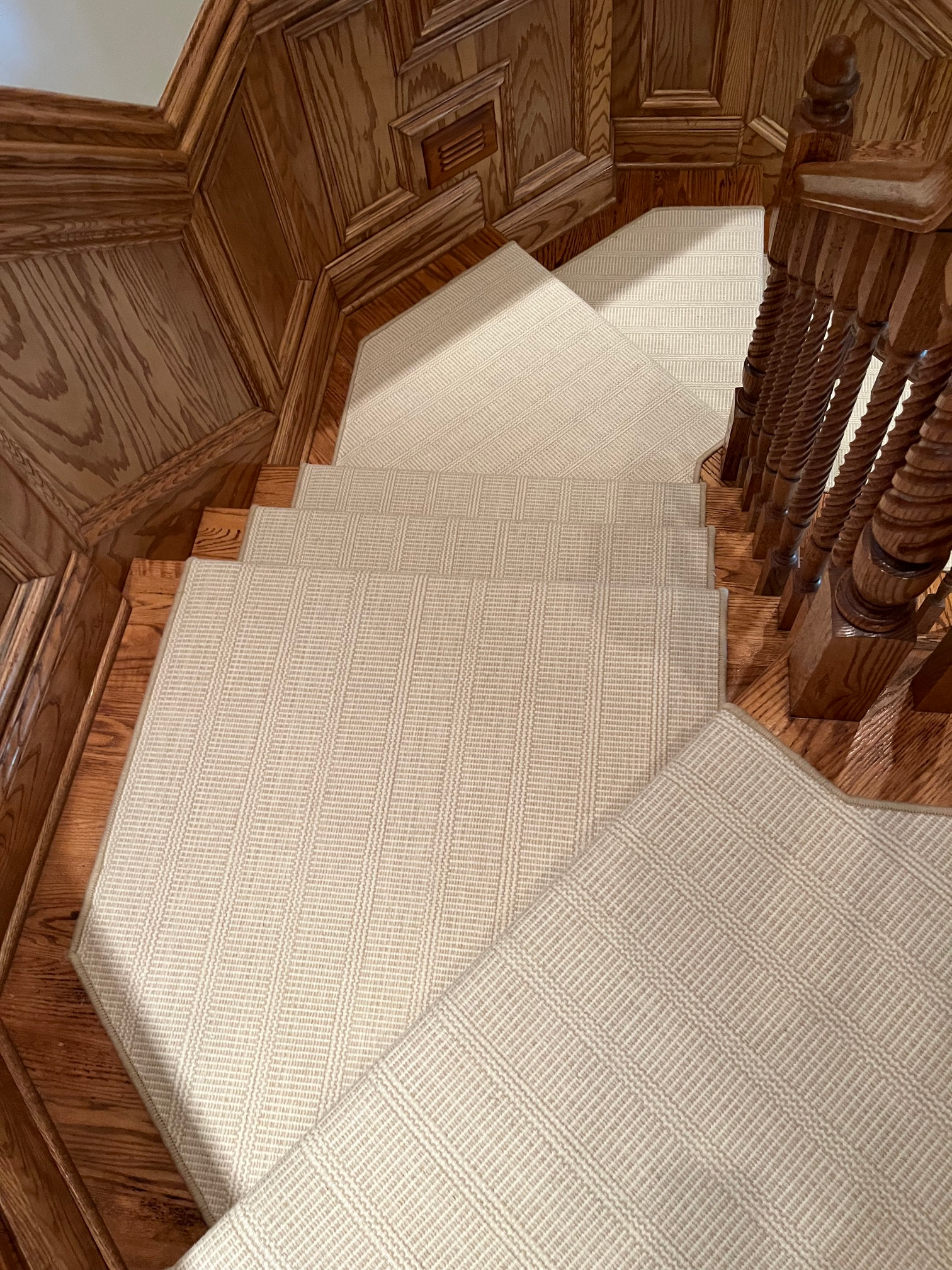 Carpeted spiral staircase with carved wooden railing and paneled walls