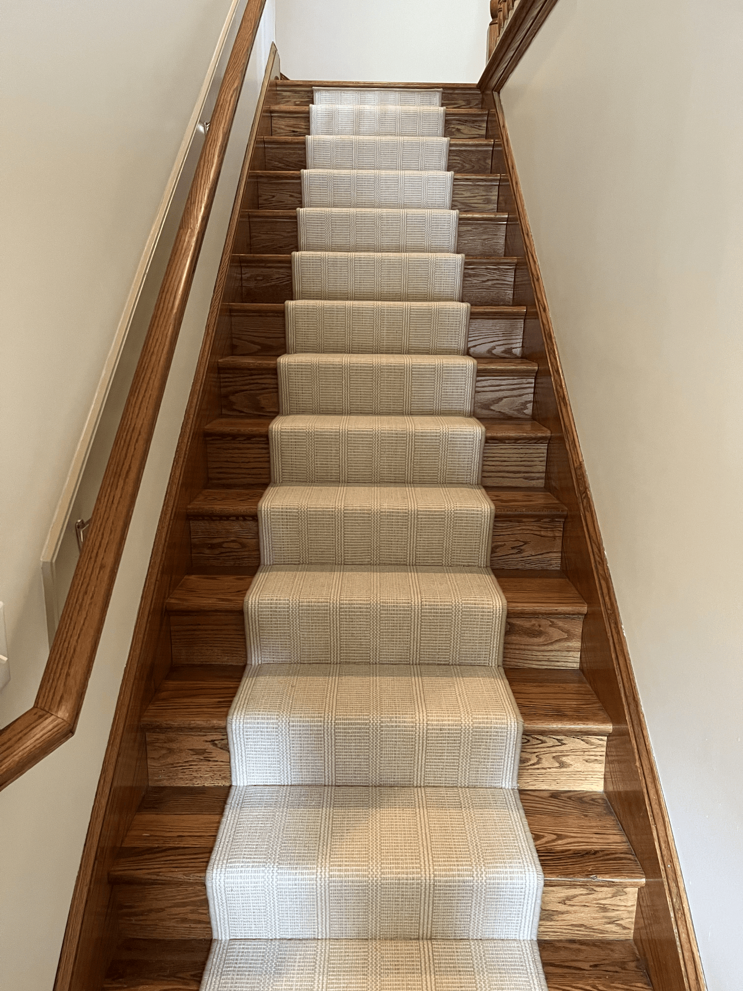 Narrow wooden staircase with beige carpet runner and handrails on both sides.