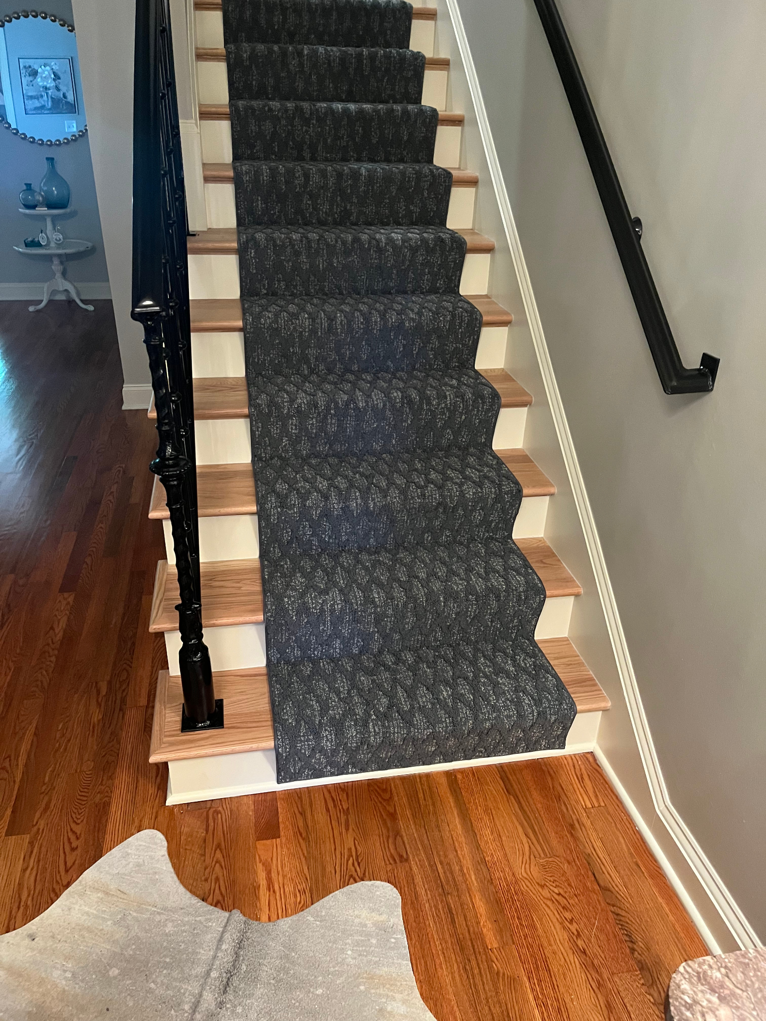 Carpeted staircase with dark gray carpet, wooden steps, and a black handrail.
