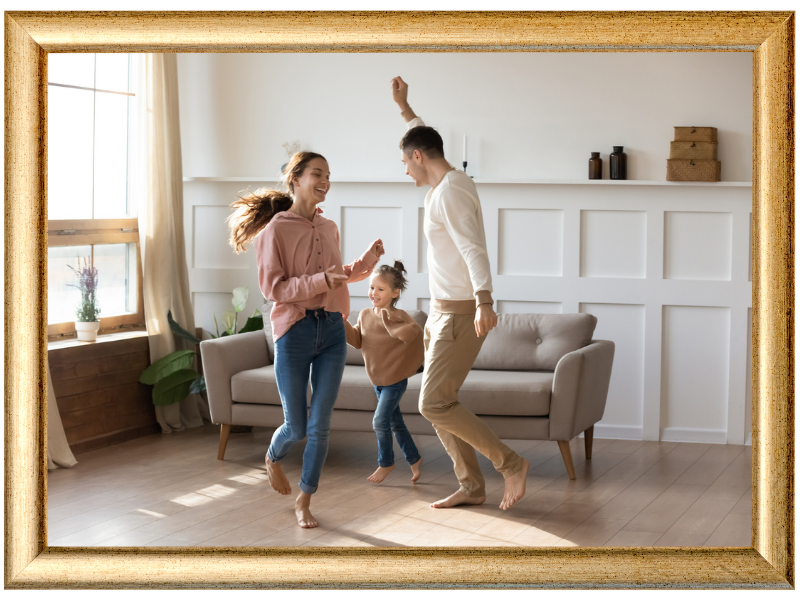 Three people dancing in a bright living room with beige chairs and white paneled walls.