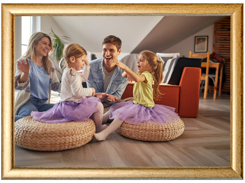 Family sitting on floor cushions in a cozy living room, smiling and interacting around a laptop.