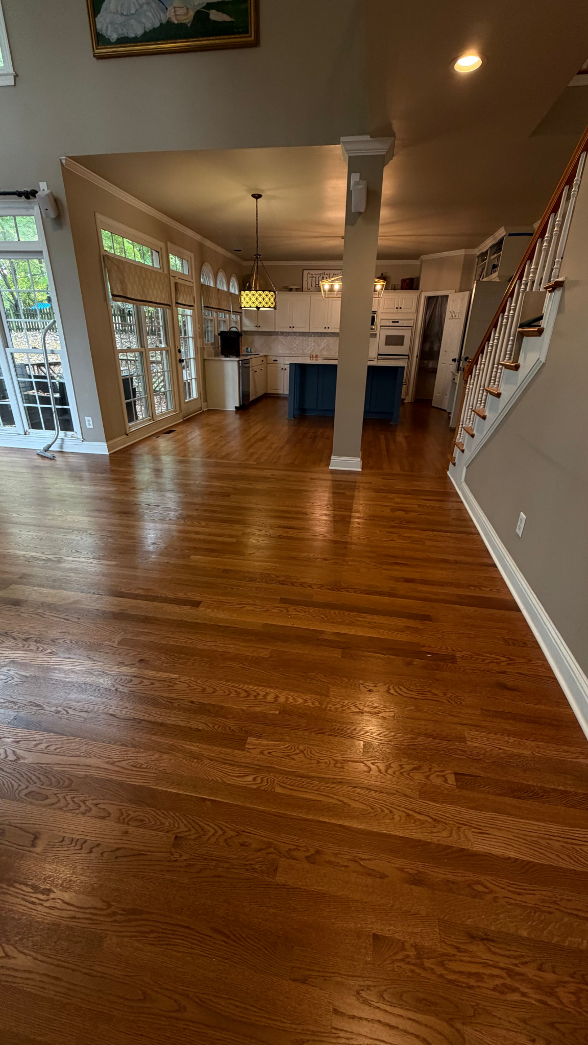 Spacious empty living room with hardwood floors, white columns, and a staircase along the right wall.