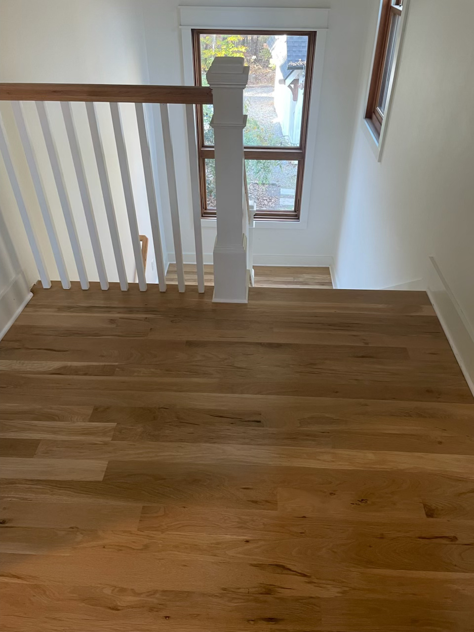 Wooden upstairs landing with white railing and a window at the end of the hall