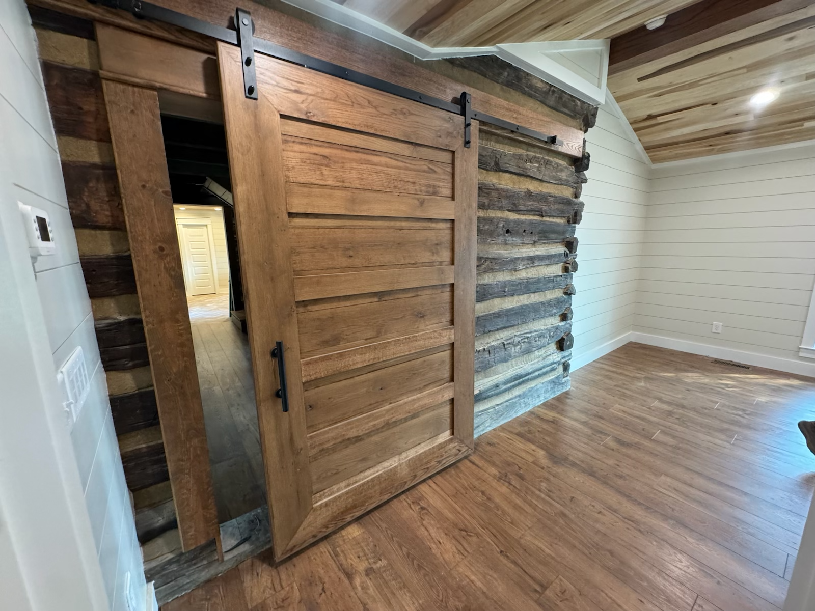 Rustic sliding barn door on a log wall, opening into a room with hardwood floors.
