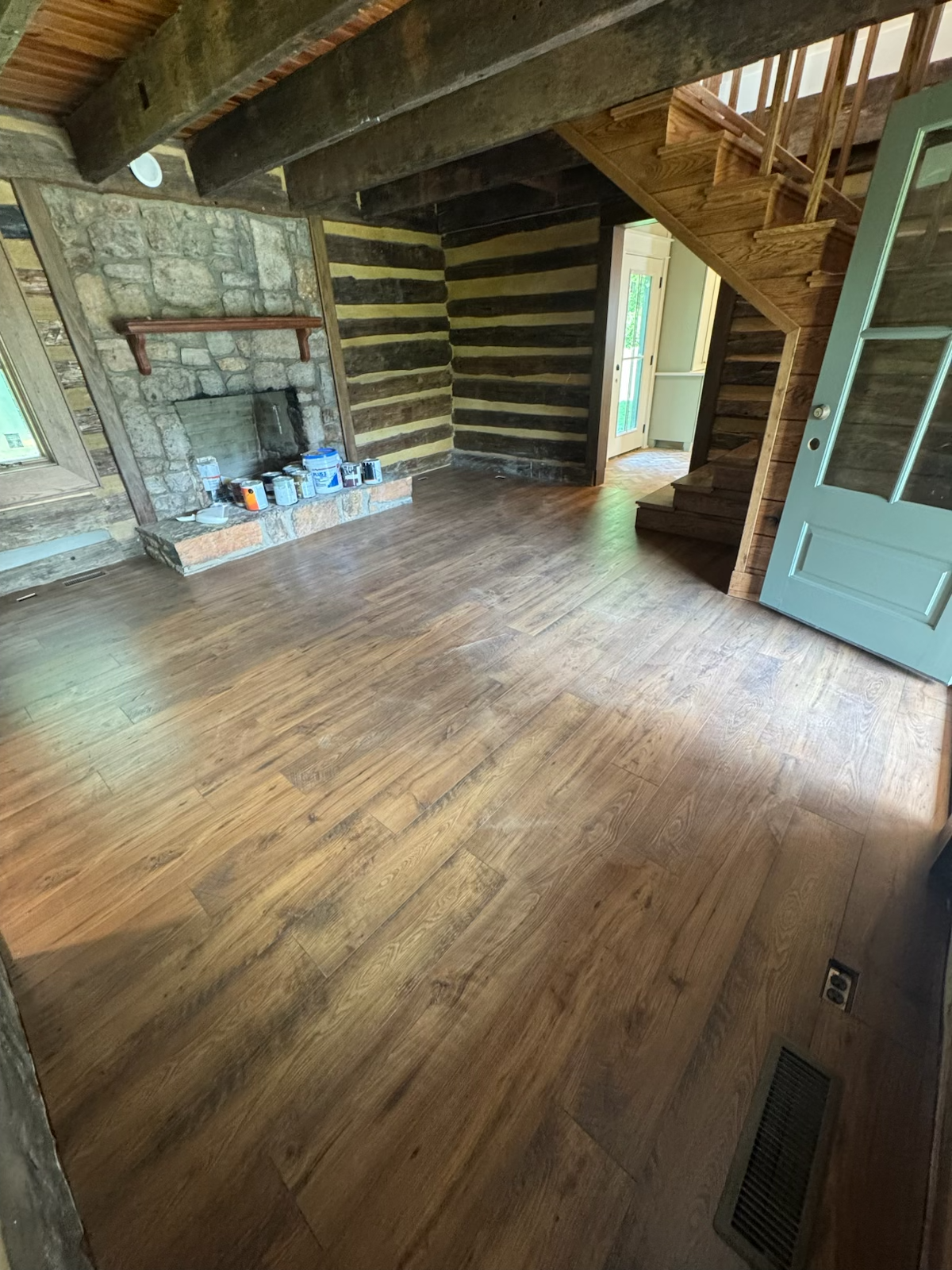 Spacious log cabin interior with stone fireplace, wooden floors, and staircase.