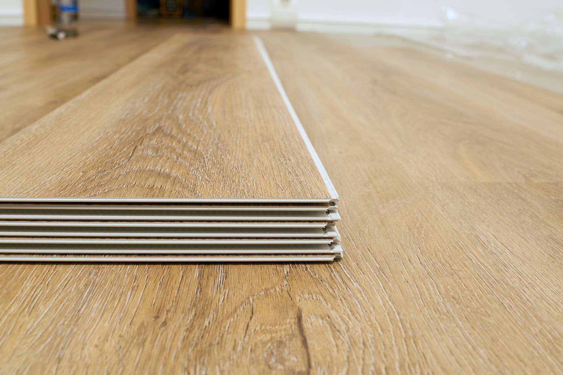 Stack of light brown planks beside installed wood-look flooring, likely for a floor renovation.