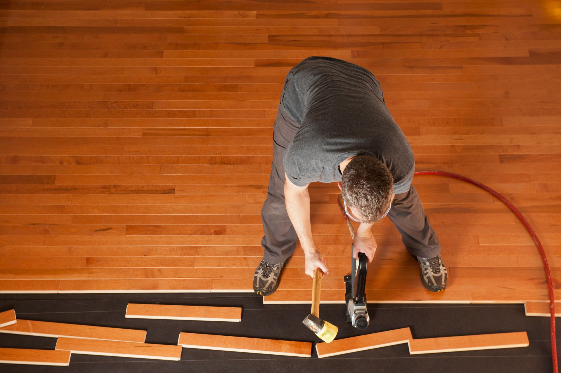 Man installing hardwood flooring, using a hammer and nail gun.