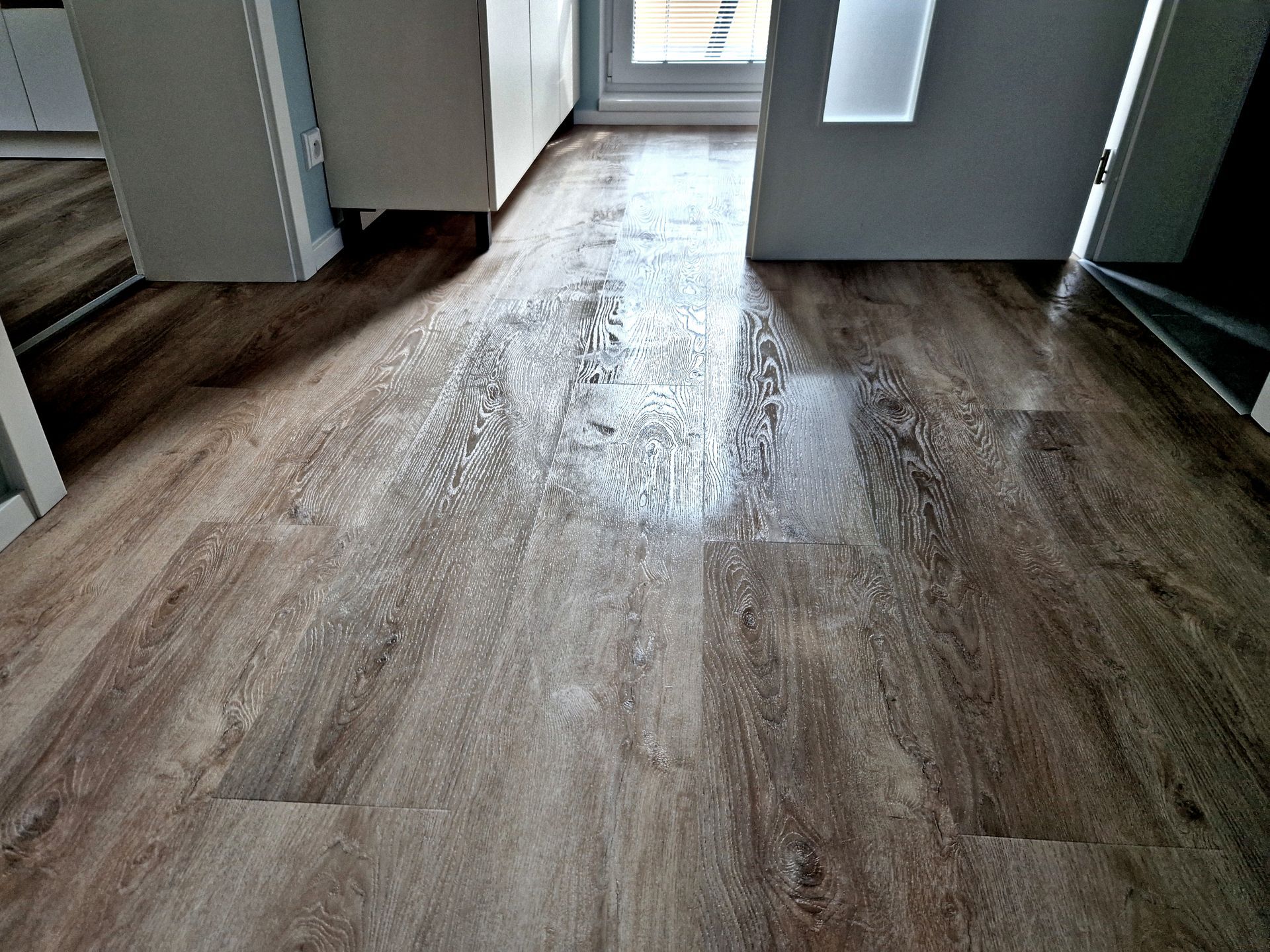 Empty hallway with wood flooring leading to a bright doorway.
