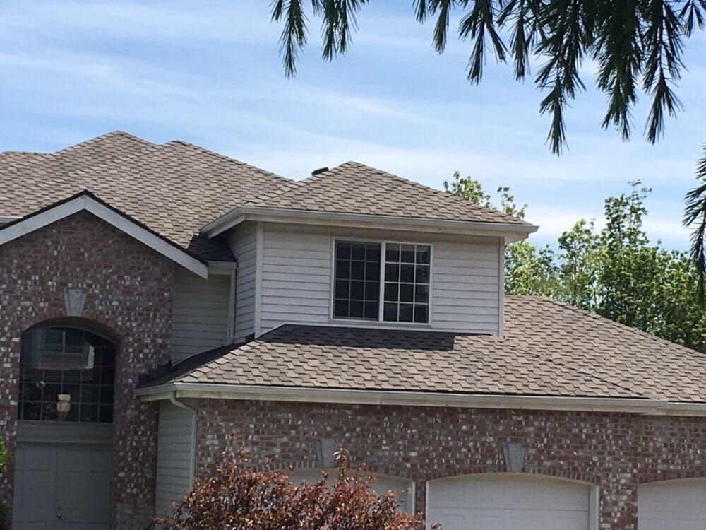 Suburban house exterior with brick and siding, shingled roof, and trees overhead