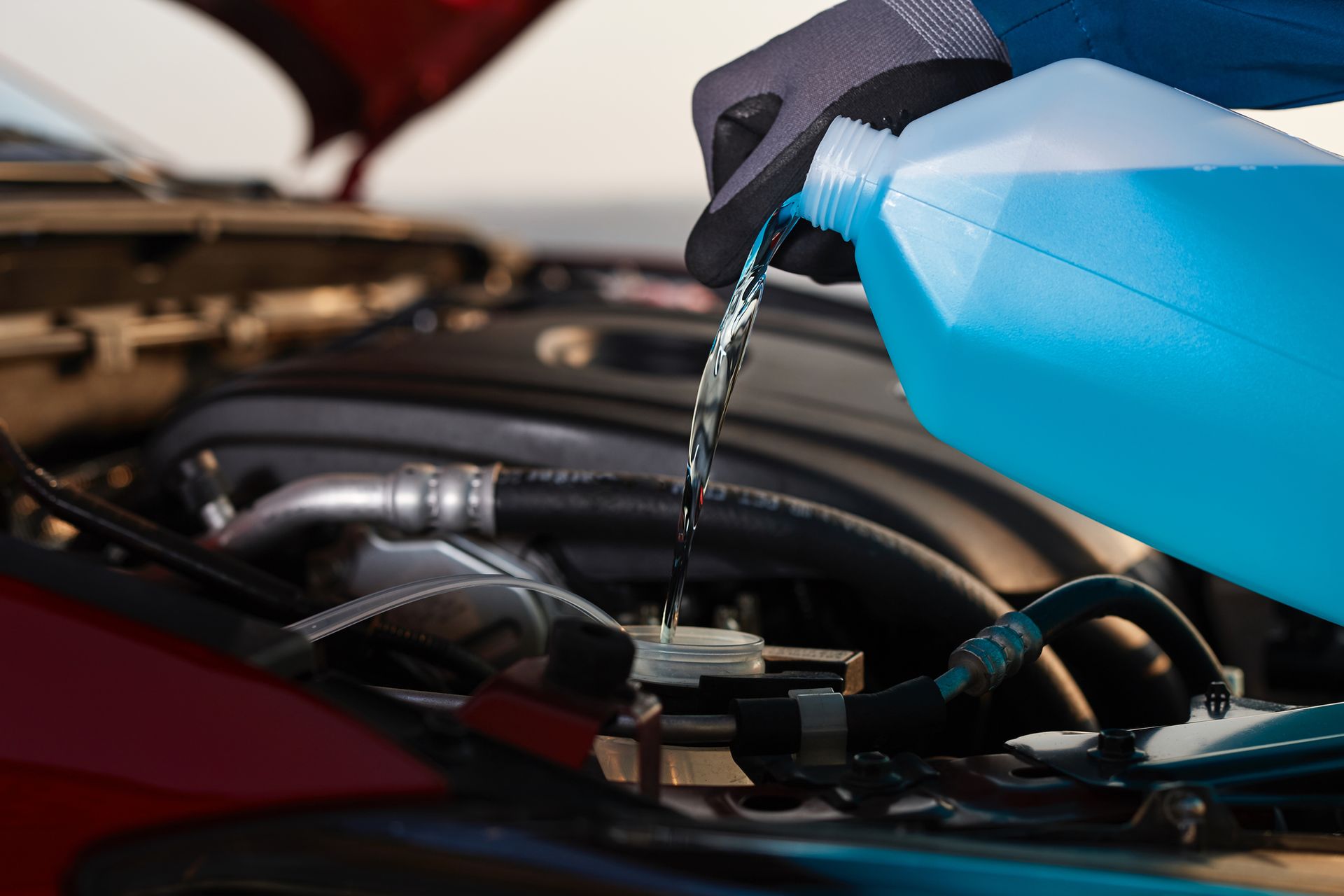 Person pouring blue fluid from a jug into a car's engine compartment.