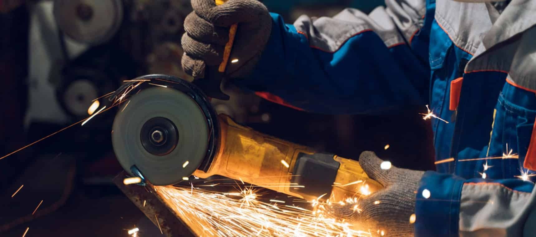 A Man is Grinding a Piece of Metal With a Grinder — Top End Steel Supplies Darwin In Alice Springs, NT