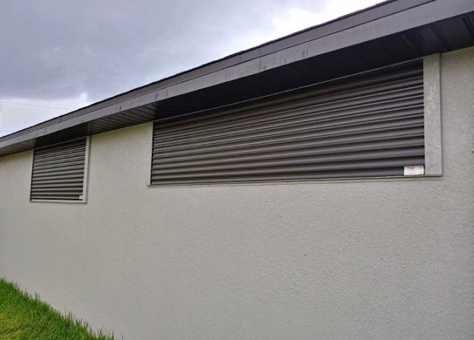There are two windows on the side of a building with shutters on them.