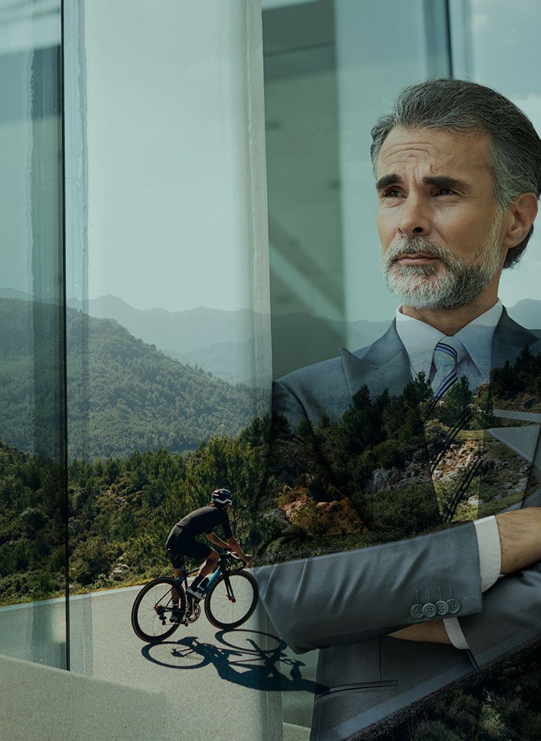 Man in suit looks out at cyclist on a mountain road. Overlaid image of the landscape.
