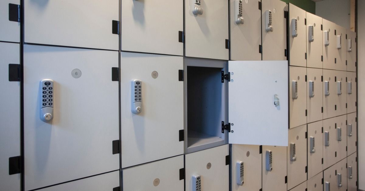 White locker doors with silver keypad locks and black hinges lining a wall, with one open empty.