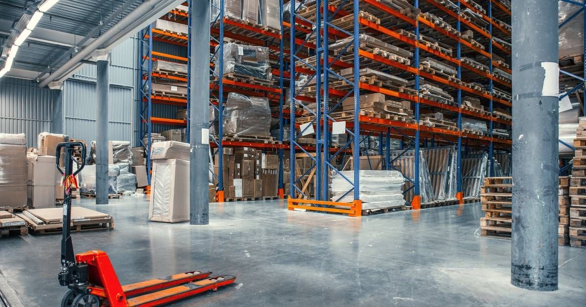 The interior of a warehouse is full of wooden pallets. A forklift is parked beside the pallet racks.