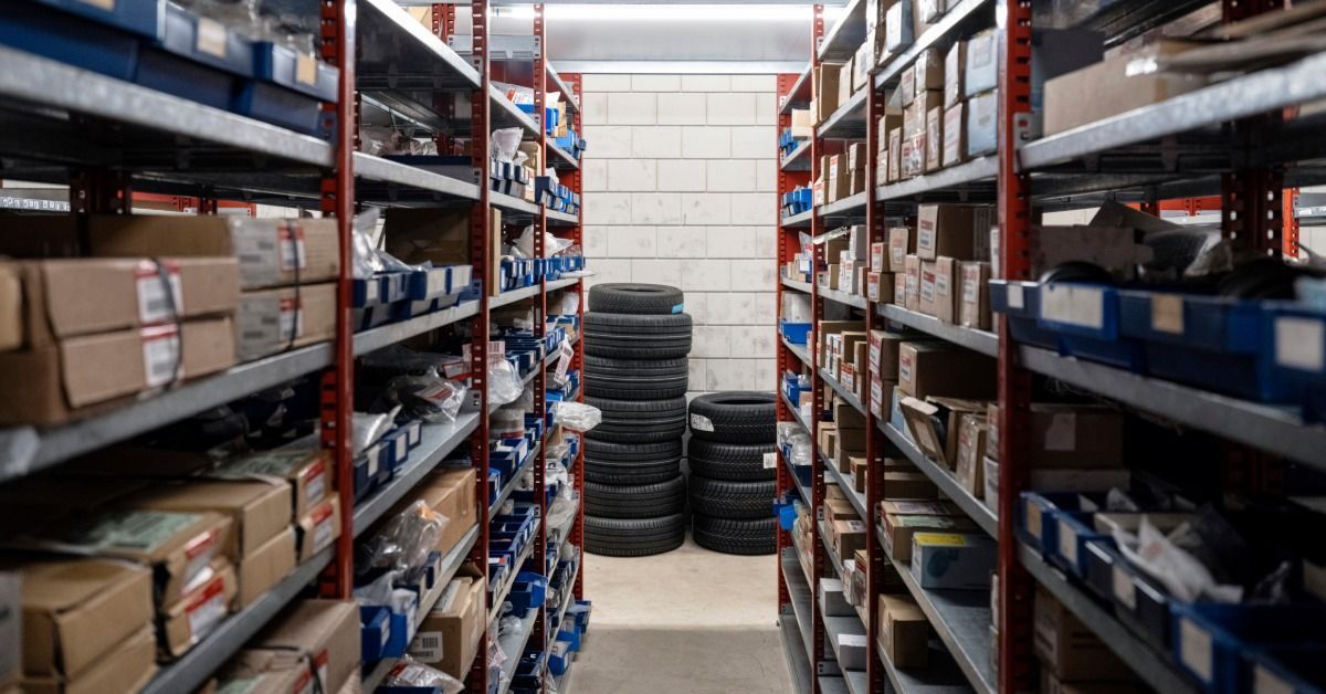 A row of shelves in an automotive facility. Each shelf has packages, and there are stacked tires past the shelves.