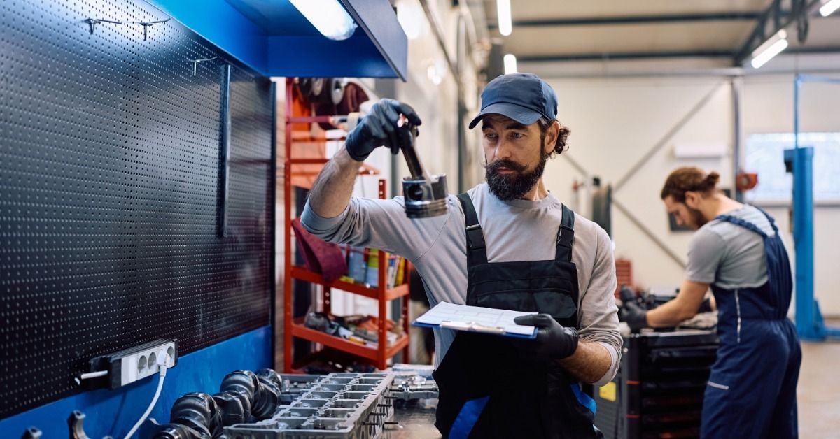 A car mechanic examining vehicle parts on a workbench in an auto repair shop. The workbench wall is empty.