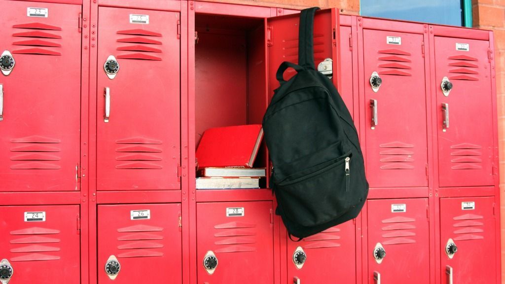 A row of school lockers with one of them open. The open locker has a backpack hanging off the door and books inside.