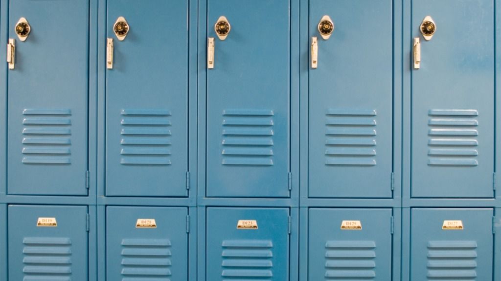 Two shelves of blue school lockers with all of them closed. All of the lockers have a lock above the handles.