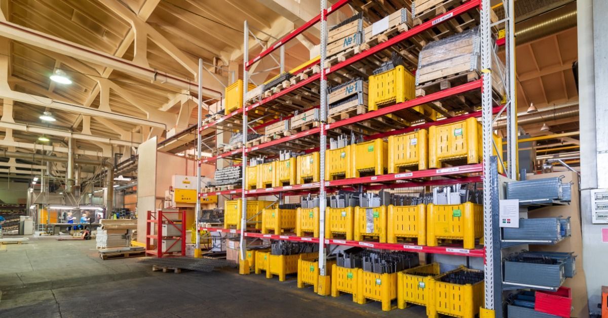 A warehouse shelf holds large yellow plastic bins and stacked metal reinforcement materials inside an industrial space.