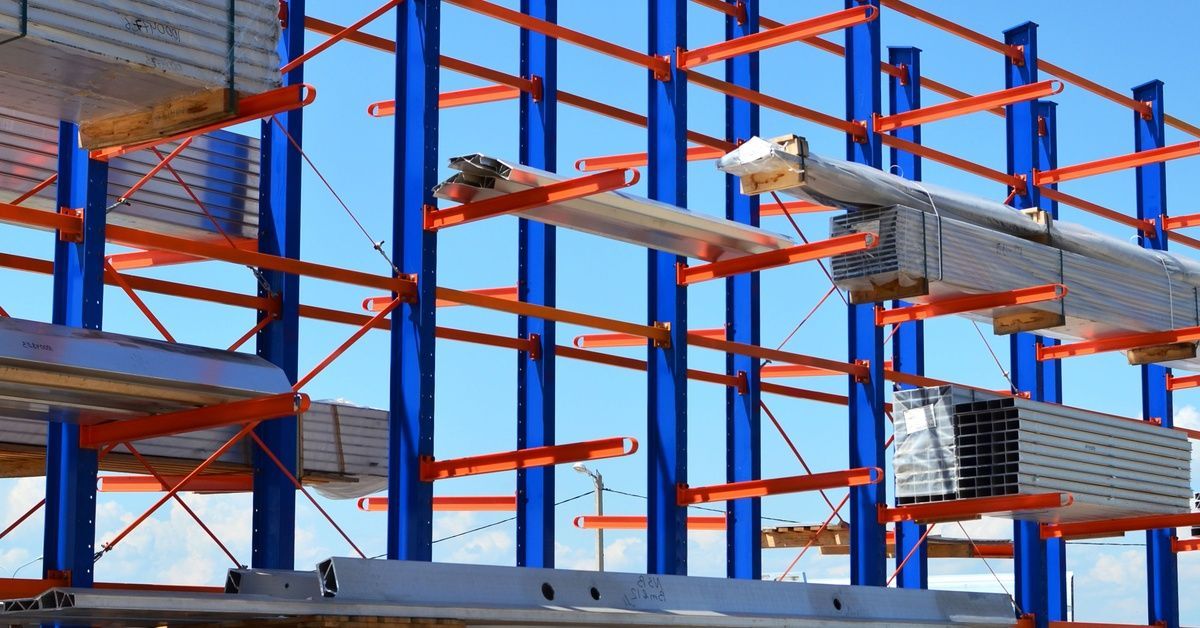 An outdoor facility with cantilever racks holding various items, including long metal profiles, pipes, and sheet metal.