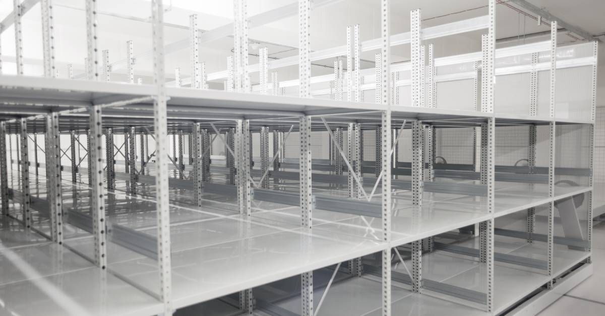 A cluster of empty white industrial steel shelving units in the basement of a warehouse lit with fluorescent light.