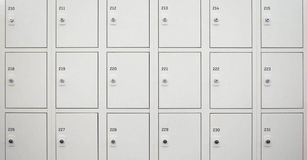 A close-up view of small employee lockers, made from metal and triple-stacked. Each locker is numbered 210 to 231.