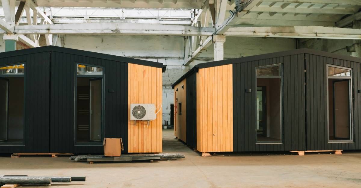 Two prefabricated modular office structures set up inside of an industrial warehouse building. One structure has HVAC equipment.
