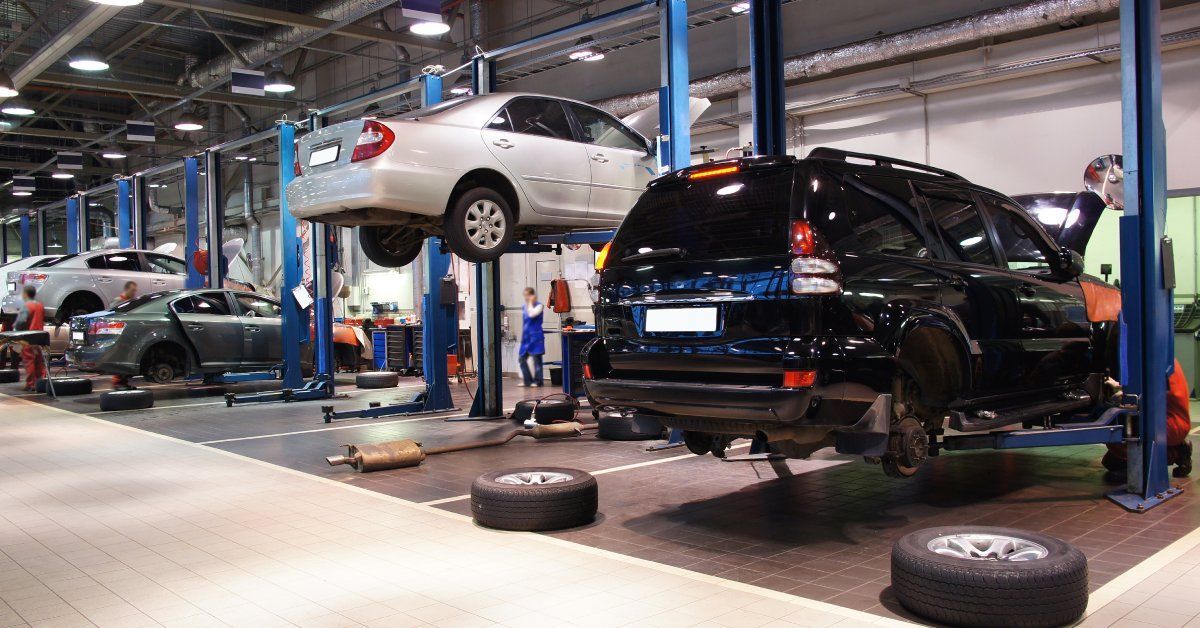 A row of blue in-ground car lifts inside of an auto shop. Three cars are suspended in the air and one is on the ground.